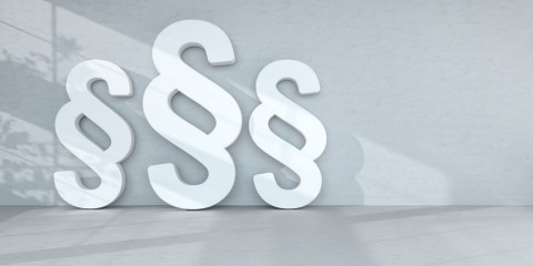 Drei weiße Paragraphensymbole auf hellem Hintergrund.