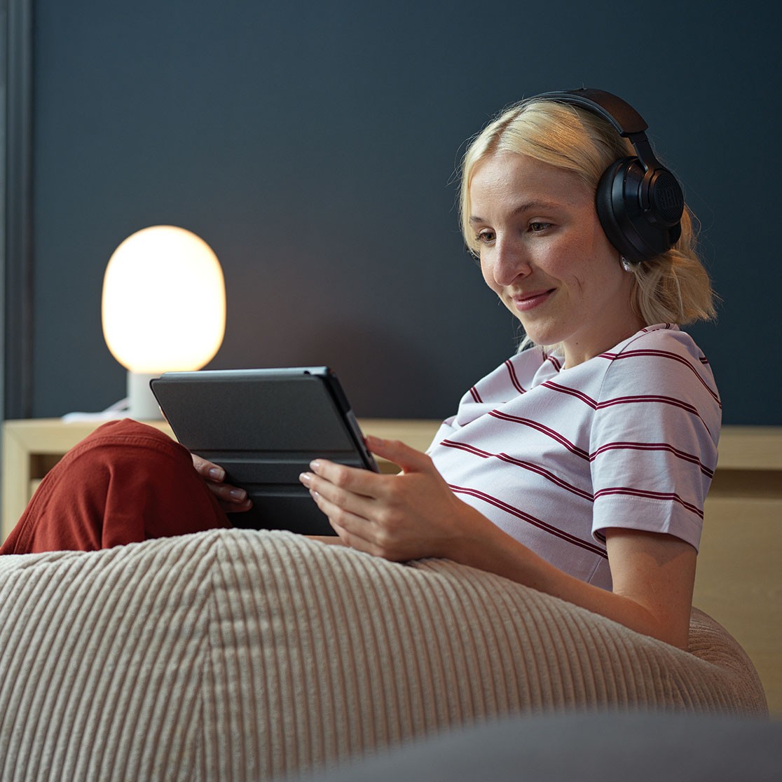 Frau sitzt auf einem Sessel und schaut lächeln in ihr Tablet.