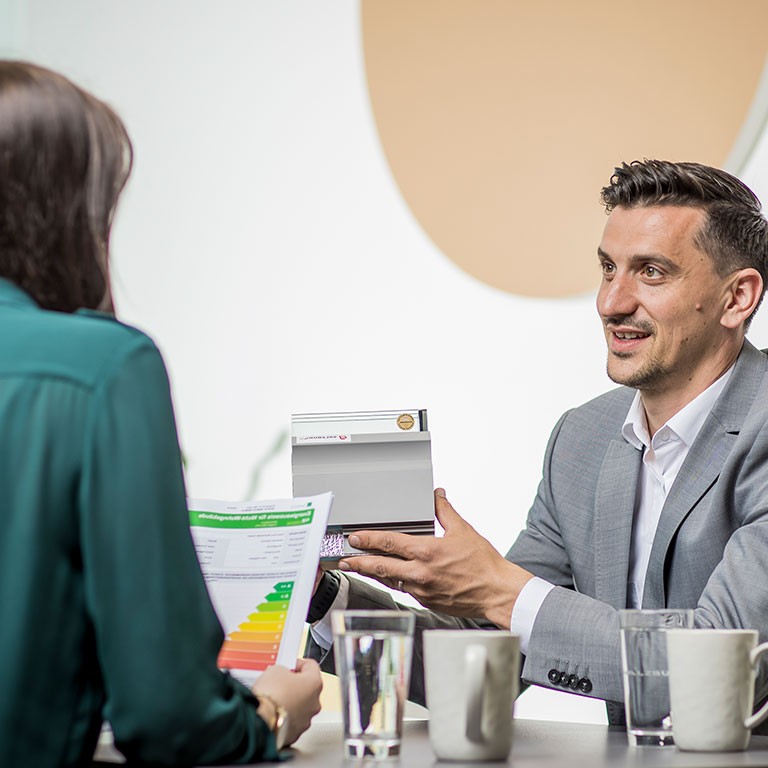 Beratungstermin: Mitarbeiter präsentiert Kundin Unterlagen.