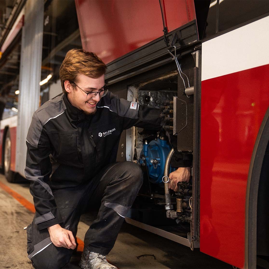 Lehrling in Salzburg-AG-Arbeitskleidung bei Wartung an einem roten Bus