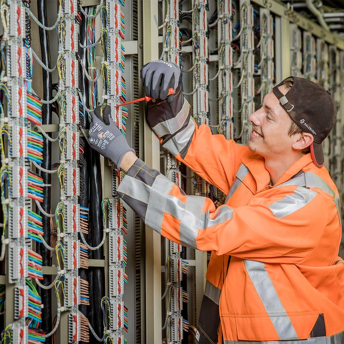 Person in Warnkleidung arbeitet mit Werkzeug an Kabeln in einem Serverraum