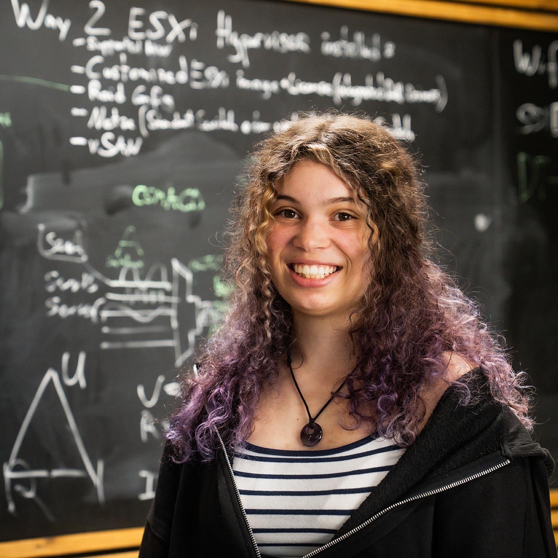 Junge Frau steht vor einer Kreidetafel und blickt lächelnd in die Kamera