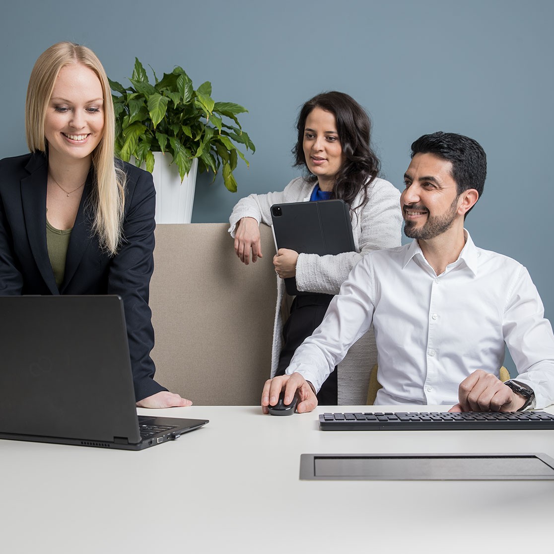 Drei Mitarbeiter:innen der Salzburg AG stehen gemeinsam am Schreibtisch