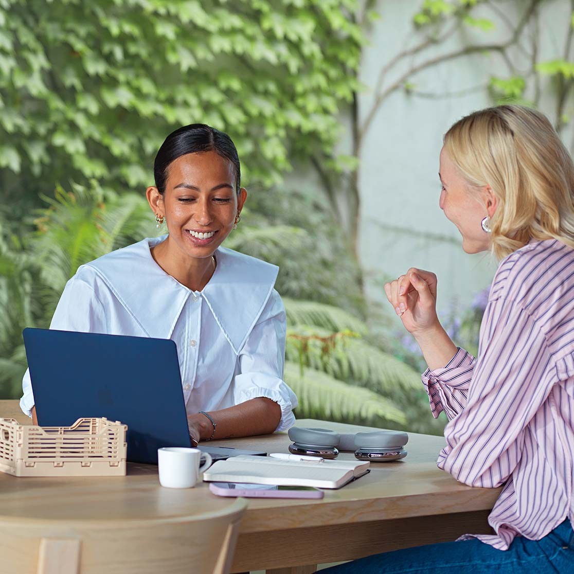 Zwei Frauen unterhalten sich und haben einen geöffneten Laptop vor sich.