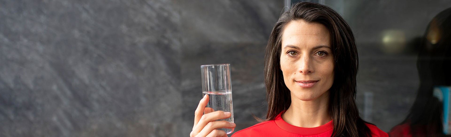 Glas mit Wasser in der Hand einer lächelnden Frau.