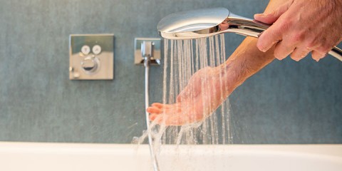 Hand unter Duschkopf mit Wasserstrahlen.